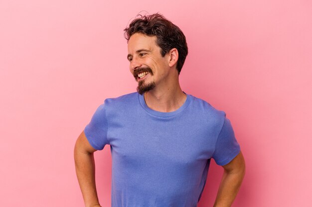 Young caucasian man isolated on pink background confident keeping hands on hips.
