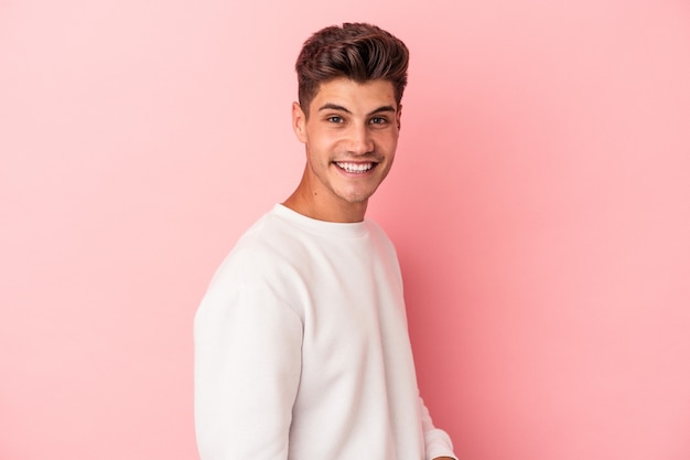 Young caucasian man isolated on pink background confident keeping hands on hips.