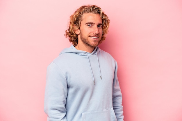 Young caucasian man isolated on pink background confident keeping hands on hips.