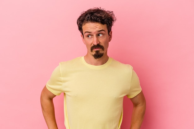 Young caucasian man isolated on pink background confused, feels doubtful and unsure.