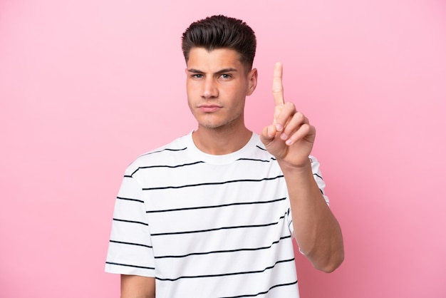 Young caucasian man isolated on pink background counting one with serious expression