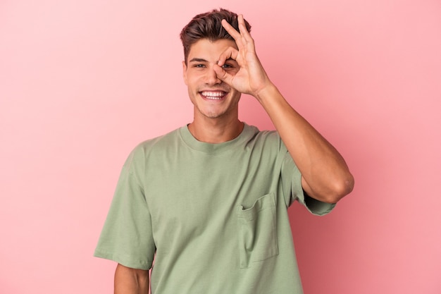 Young caucasian man isolated on pink background excited keeping ok gesture on eye.