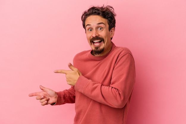 Young caucasian man isolated on pink background excited pointing with forefingers away.