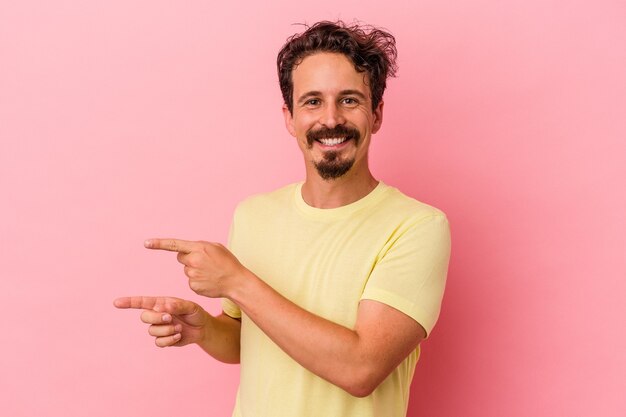 Young caucasian man isolated on pink background excited pointing with forefingers away.