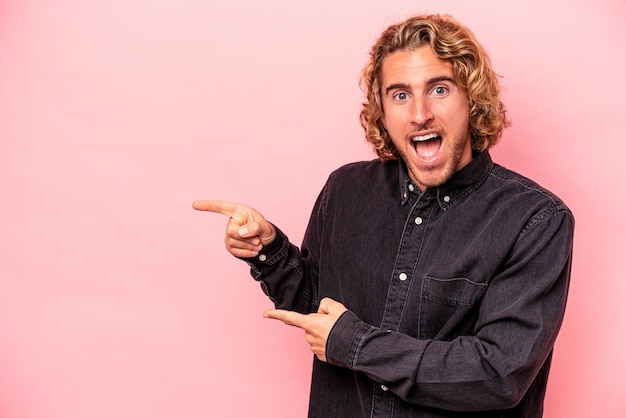 Photo young caucasian man isolated on pink background excited pointing with forefingers away.