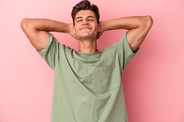 Young caucasian man isolated on pink background feeling confident, with hands behind the head.