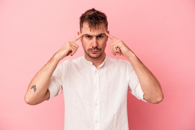 Young caucasian man isolated on pink background focused on a task, keeping forefingers pointing head.