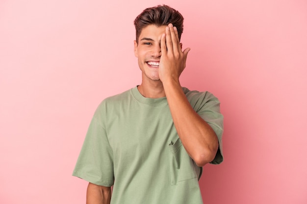 Young caucasian man isolated on pink background having fun covering half of face with palm.
