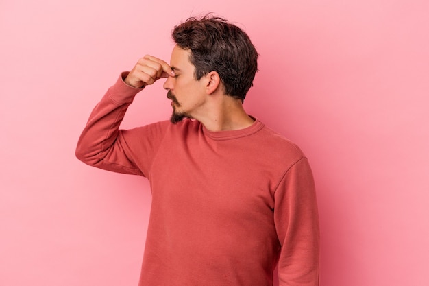 Young caucasian man isolated on pink background having a head ache, touching front of the face.
