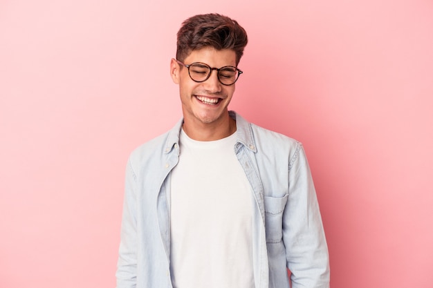 Young caucasian man isolated on pink background laughs and closes eyes, feels relaxed and happy.