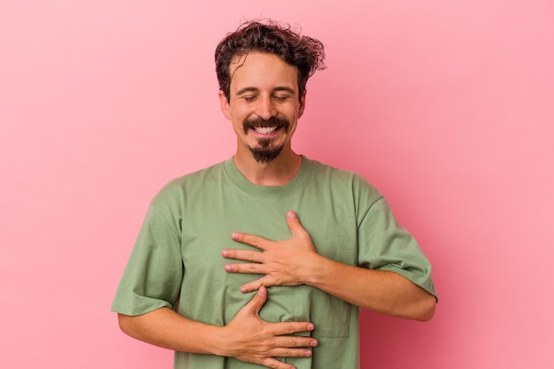 Young caucasian man isolated on pink background laughs happily and has fun keeping hands on stomach.