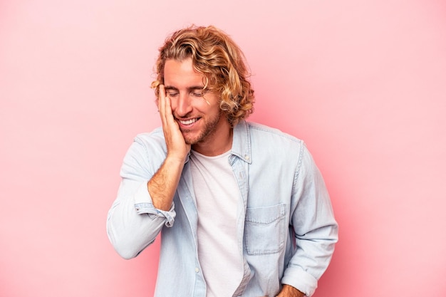 Young caucasian man isolated on pink background laughs happily and has fun keeping hands on stomach.