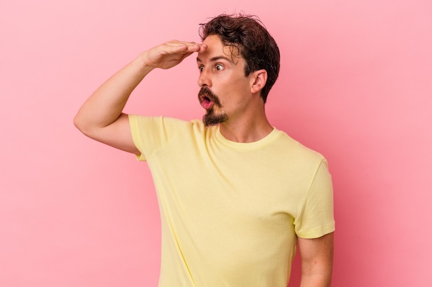 Young caucasian man isolated on pink background looking far away keeping hand on forehead.