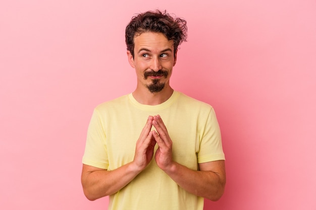 Young caucasian man isolated on pink background making up plan in mind, setting up an idea.