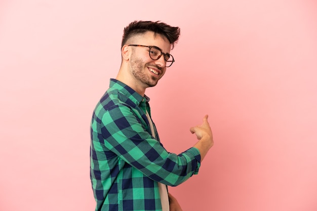 Young caucasian man isolated on pink background pointing back