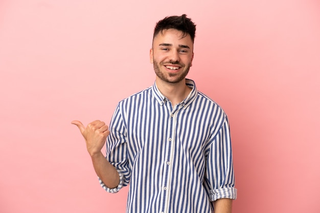 Young caucasian man isolated on pink background pointing to the side to present a product