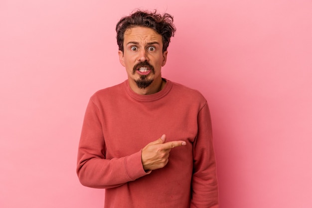 Young caucasian man isolated on pink background pointing to the side