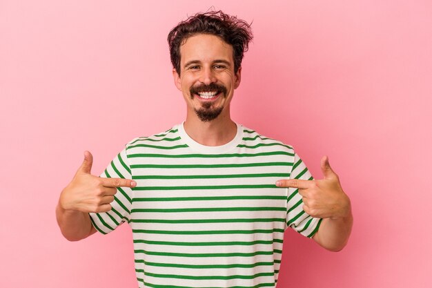 Young caucasian man isolated on pink background points down with fingers, positive feeling.