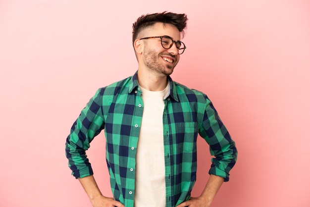 Young caucasian man isolated on pink background posing with arms at hip and smiling