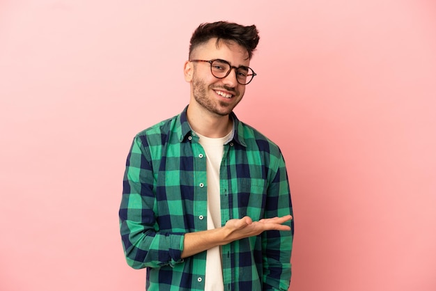 Young caucasian man isolated on pink background presenting an idea while looking smiling towards