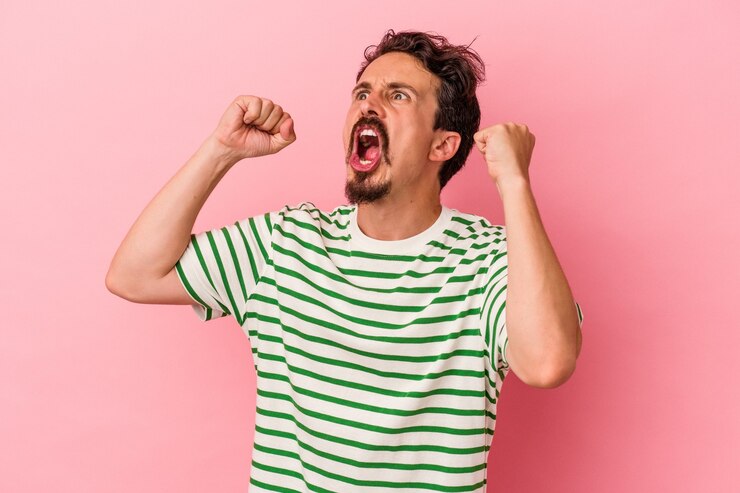 Photo young caucasian man isolated on pink background raising fist after a victory, winner concept.