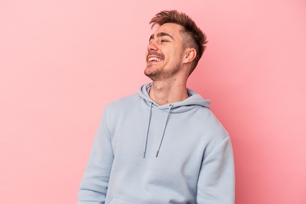 Young caucasian man isolated on pink background relaxed and happy laughing, neck stretched showing teeth.