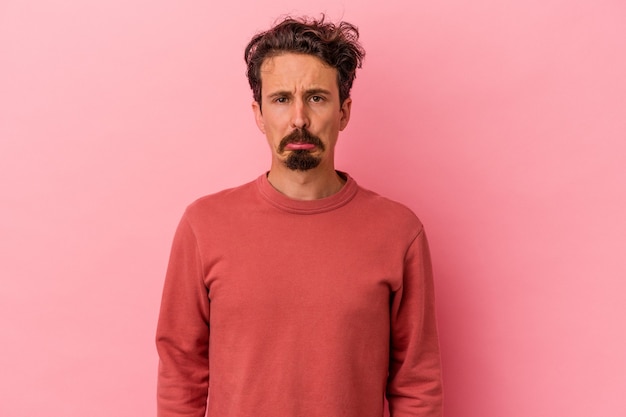 Young caucasian man isolated on pink background sad, serious face, feeling miserable and displeased.