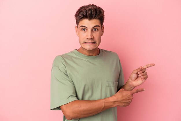 Young caucasian man isolated on pink background shocked pointing with index fingers to a copy space.