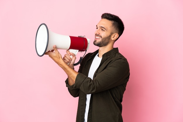 Young caucasian man isolated on pink background shouting through a megaphone to announce something