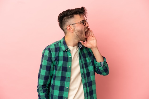 Young caucasian man isolated on pink background shouting with mouth wide open to the side