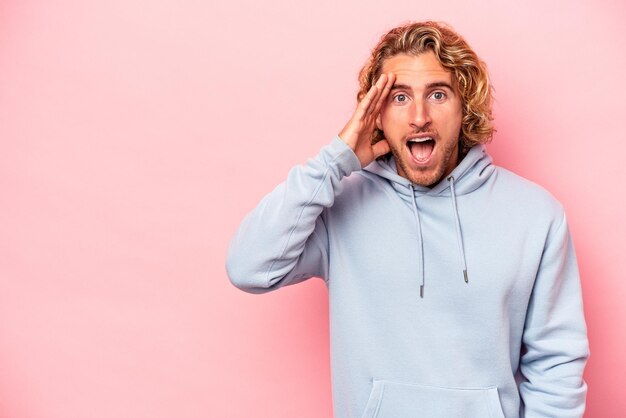 Young caucasian man isolated on pink background shouts loud, keeps eyes opened and hands tense.