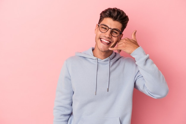 Young caucasian man isolated on pink background showing a mobile phone call gesture with fingers.