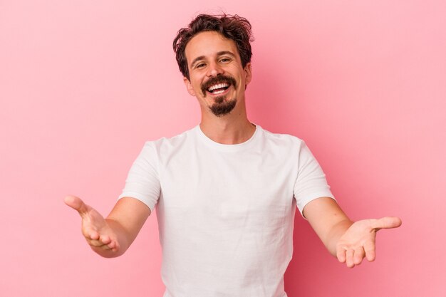 Young caucasian man isolated on pink background showing a welcome expression.