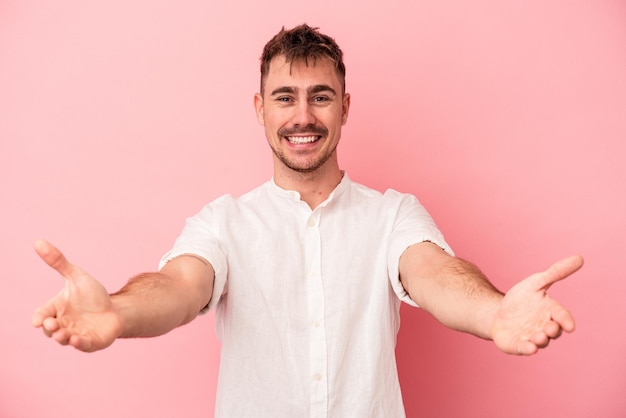 Young caucasian man isolated on pink background showing a welcome expression.