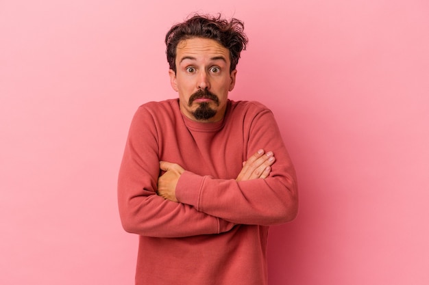 Young caucasian man isolated on pink background shrugs shoulders and open eyes confused.