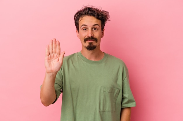 Young caucasian man isolated on pink background smiling cheerful showing number five with fingers.