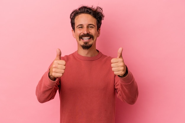 Young caucasian man isolated on pink background smiling and raising thumb up