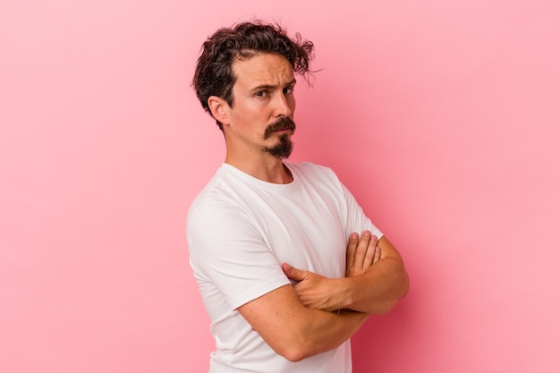 Young caucasian man isolated on pink background suspicious, uncertain, examining you.