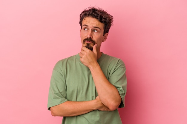 Foto giovane uomo caucasico isolato su sfondo rosa pensando e alzando lo sguardo, essendo riflessivo, contemplando, avendo una fantasia.