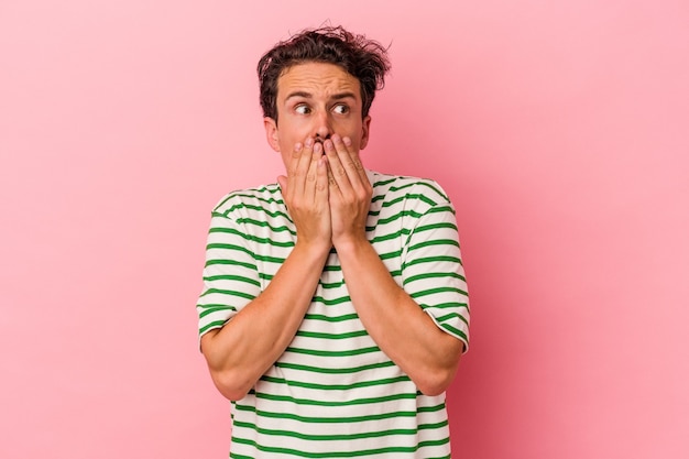 Young caucasian man isolated on pink background thoughtful looking to a copy space covering mouth with hand.