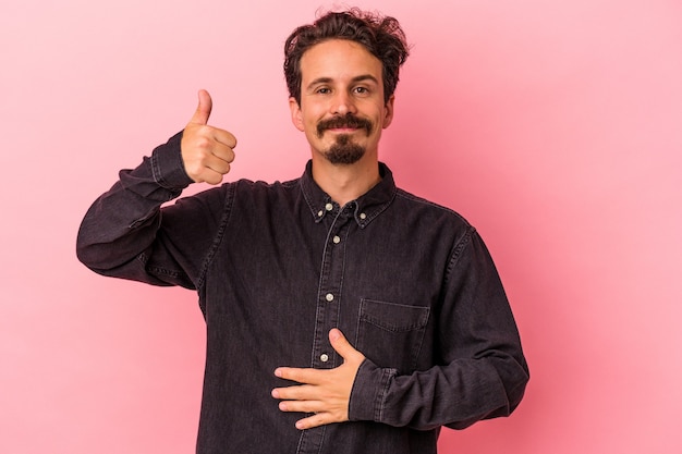 Young caucasian man isolated on pink background touches tummy, smiles gently, eating and satisfaction concept.