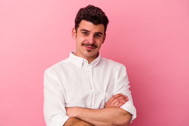 Young caucasian man isolated on pink background who feels confident, crossing arms with determination.