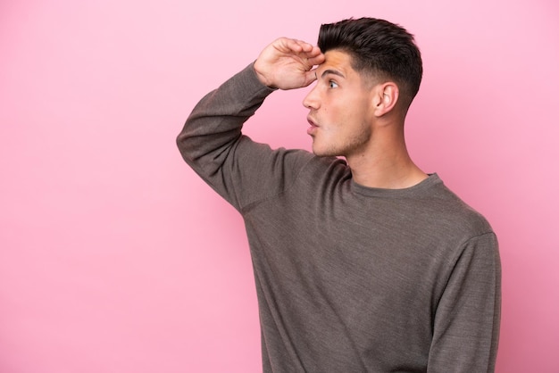 Young caucasian man isolated on pink background with surprise expression while looking side