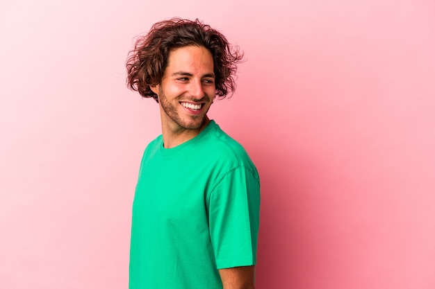 Young caucasian man isolated on pink bakcground looks aside smiling, cheerful and pleasant.