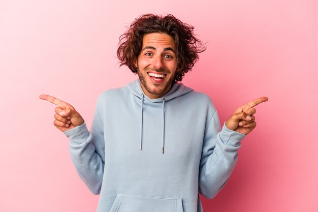 Young caucasian man isolated on pink bakcground pointing to different copy spaces, choosing one of them, showing with finger.