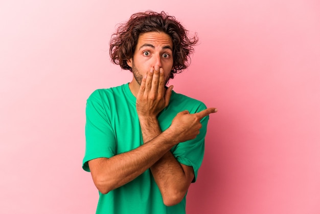 Young caucasian man isolated on pink bakcground pointing to the side