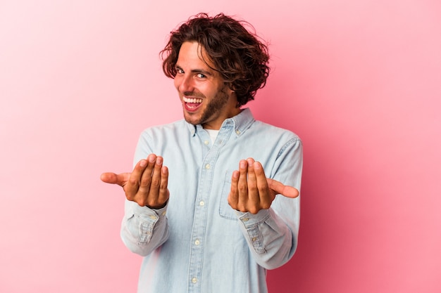 Young caucasian man isolated on pink bakcground pointing with finger at you as if inviting come closer.