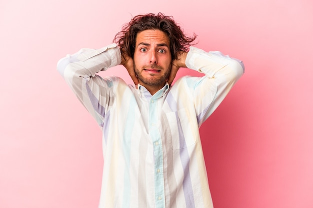 Young caucasian man isolated on pink bakcground screaming with rage.