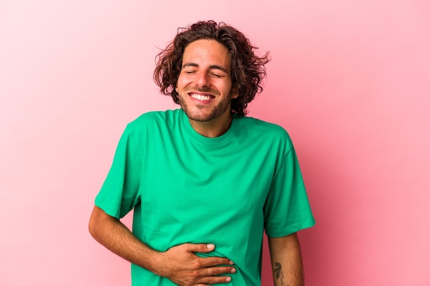 Young caucasian man isolated on pink bakcground touches tummy, smiles gently, eating and satisfaction concept.