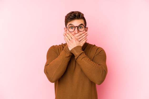 Young caucasian man isolated on pink shocked covering mouth with hands.